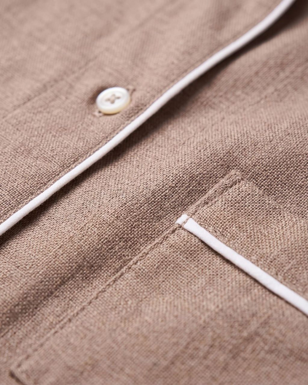 Close-up of brown cotton pajama fabric, button, white piping and chest pocket