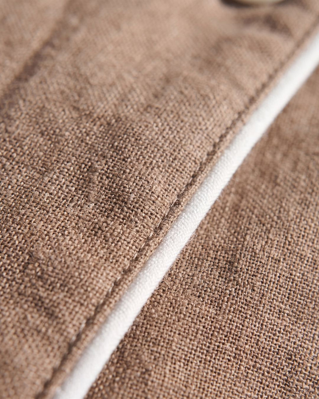 Close-up of brown cotton fabric texture and contrast white piping