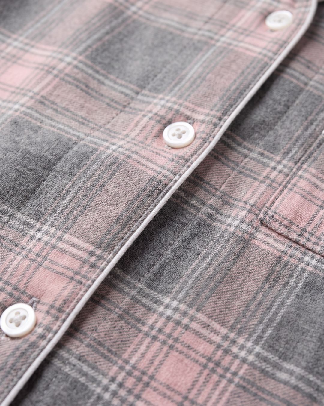 Close-up of gray plaid flannel fabric with subtle pink accents and white piping